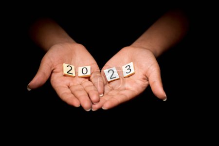 Photo for Hands of young female woman with tokens forming the number 2023 on black background - Royalty Free Image