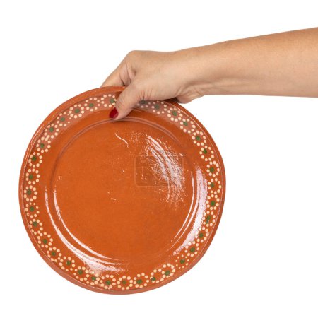 Foto de Woman's hand Oval red clay plate made in Mexico. Traditional handmade Mexican clay crockery. isolated White background. - Imagen libre de derechos