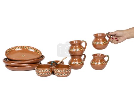 Photo for Woman's hand with Tableware of several pieces of red clay made in Mexico. Traditional handmade Mexican clay crockery. isolated White background. - Royalty Free Image
