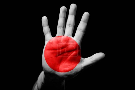 Rude man hand with flag of Japan in stop sign to anger, discrimination, racism, abuse on black background.