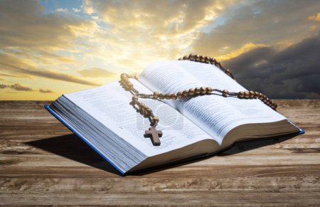 Hopen holy bible and rosary on wooden table and sunset background.