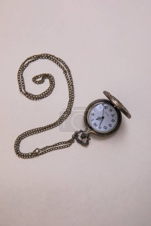 old pocket watch with train engraving on the cover, patinated brobce color, open with chain arranged in a spiral on beige background overhead view