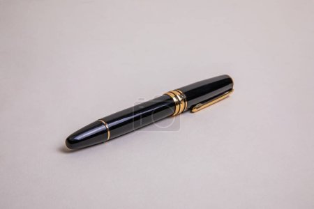 elegant black metal fountain pen with gold details 3/4 low angle view on beige background