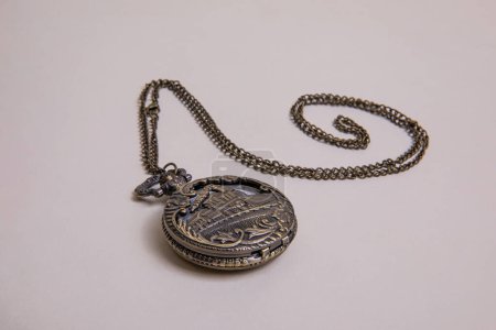 old pocket watch with train engraving on the cover, patinated brobce color, closed with chain arranged in a spiral on a beige background overhead view