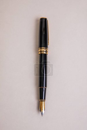 elegant black metal fountain pen with gold details in overhead view on beige background