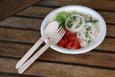 Photo for Detail of wooden disposable cutlery with food in chinet disposable bowl on wooden table - takeaway food concept, eco friendly, space for text - Royalty Free Image