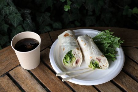 Photo for Food take out - concept - chicken torilla on a chinet disposable paper plate, bamboo finger fodd skewers and a drink in a bio disposable cup on a wooden table with space for text - Royalty Free Image