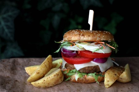 Hamburger mit Käse, Gemüse, Kartoffeln und Bambus-Fingerfood-Stick auf einem Tisch mit dunklem Hintergrund und Platz für Text. Takeaway, take out Konzept. Rustikaler Stil.