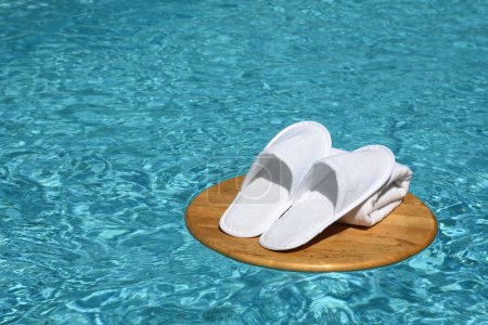 Photo for Close up view of white slippers ad towels on wooden circle in pool. Balneo, spa, hotel, home concept - Royalty Free Image