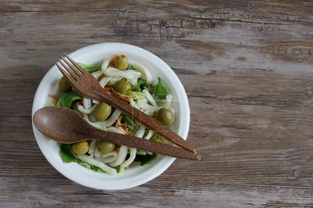 Téléchargez les photos : Salade de pâtes fraîches dans une assiette compostable jetable, couverts marrons biodégradables écologiques jetables sur une table en bois avec espace pour le texte concept de respect de l'environnement - en image libre de droit