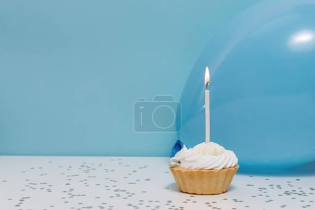 Téléchargez les photos : Gâteau d'anniversaire avec une bougie, un ballon et un décor festif sur un fond bleu uni. Contexte de votre conception - en image libre de droit