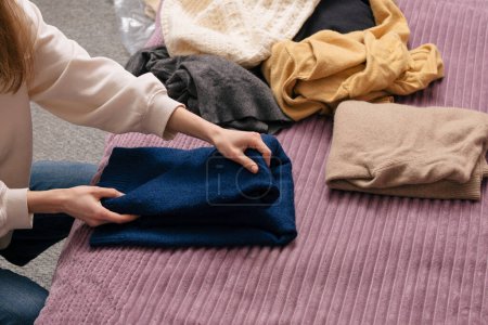 Eine junge Frau legt warme Kleidung zur Aufbewahrung ab. Das Konzept, die Garderobe zu wechseln, die Dinge zu Hause zu putzen und zu organisieren