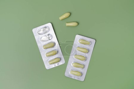 Green rectal pills or suppositories for anal or vaginal use with blister on green isolated background. Medicines for alternative medicine, lowering temperature, hemorrhoids and healthy concept