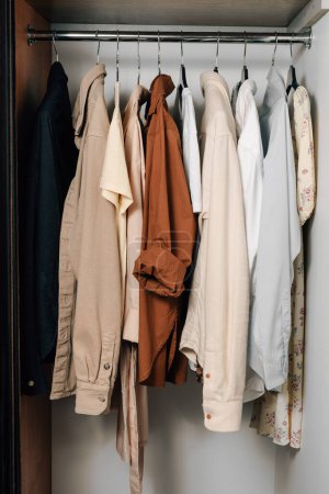 Vertikales Foto von bunten Hemden, T-Shirts und Kleidern auf Kleiderbügeln im Schrank. Das Konzept, den Kleiderschrank zu wechseln, Dinge aufzubewahren und Kleidung zu wählen