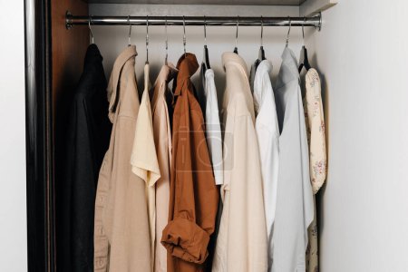 Photo for Beige, brown and white t-shirts and shirts hang on hangers in the closet. The concept of a summer wardrobe - Royalty Free Image