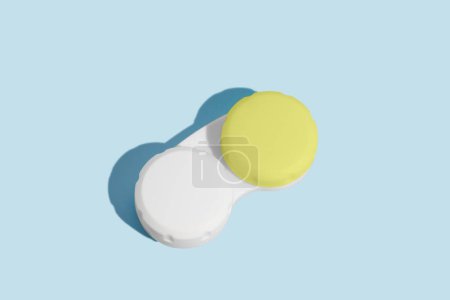 A white container with a green lid for contact lenses on a blue isolated background. Ophthalmological diseases, vision improvement concept