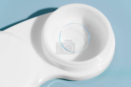 Close-up of a transparent soft contact lens in a white storage container on a blue background. Vision improvement concept, ophthalmology and treatment, eye care