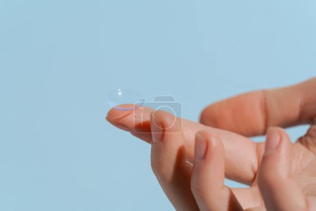Un dedo de una mano femenina sostiene una lente de contacto azul transparente sobre un fondo azul aislado. Concepto de mejora de la visión, oftalmología, clarividencia