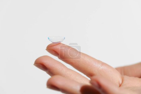 Finger der weiblichen Hand, die eine blaue, transparente Kontaktlinse auf weißem, isoliertem Hintergrund hält. Konzept der Augenheilkunde, Kurzsichtigkeit, Behandlung von Störungen, Medizin.