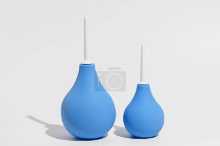Two blue rubber enemas - larger and smaller on a gray isolated background. The concept of pharmacy, medical preparations for cleansing the intestines and detoxifying the body.