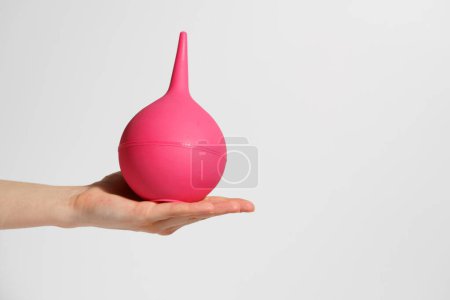 Female hand holding pink enema on white isolated background. The concept of medicine, procedures, detox and body cleansing, health topics.