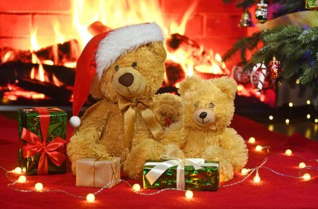 two teddy bears in santa hats hugging each other by a cozy fireplace against the backdrop of gifts and christmas lights
