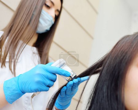 Foto de Médico cosmetólogo dermatólogo diagnostica la condición de los pacientes cabello utilizando un tricoscopio. Tricoscopia - examen por computadora del cuero cabelludo y el cabello - Imagen libre de derechos