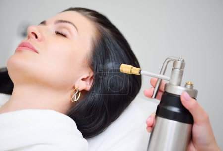 The cosmetologist makes a cryomassage of the face to the patient a cosmetological procedure of exposure to the skin with liquefied nitrogen using a cryodestructor apparatus