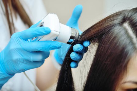 Foto de Médico cosmetólogo dermatólogo diagnostica la condición de los pacientes cabello utilizando un tricoscopio. Tricoscopia - examen por computadora del cuero cabelludo y el cabello - Imagen libre de derechos