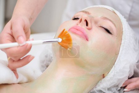 Un cosmetólogo realiza un procedimiento de terapia enzimática para una paciente femenina. El médico dermatólogo usa una máscara enzimática