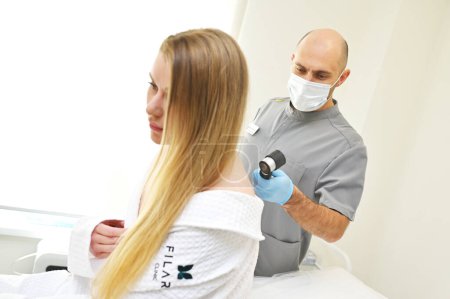Téléchargez les photos : Un dermatologue examine les tumeurs sur la peau des patients à l'aide d'un dispositif dermatoscopique spécial. Prévention du mélanome. - en image libre de droit