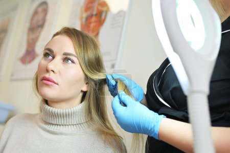 Ein Dermatologe untersucht die Haarstruktur einer jungen Patientin mit einem optischen Dermatoskop.