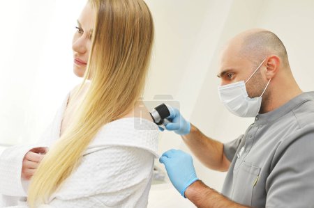 Téléchargez les photos : Un dermatologue examine les tumeurs sur la peau des patients à l'aide d'un dispositif dermatoscopique spécial. Prévention du mélanome. - en image libre de droit