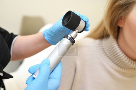 Photo for A dermatologist trichologist examines the hair structure of a young womans patient using an optical dermatoscope device. - Royalty Free Image