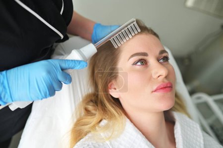 Ein Dermatologe Trichologe führt den Eingriff mit einem Darsonval-Gerät durch, um den Zustand und die Qualität der Haare der Patienten zu verbessern.