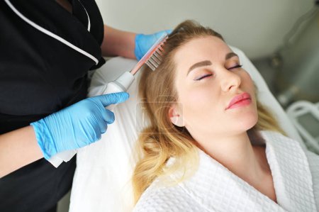 Un tricólogo dermatólogo realiza el procedimiento con un dispositivo darsonval para mejorar la condición y la calidad del cabello de los pacientes..