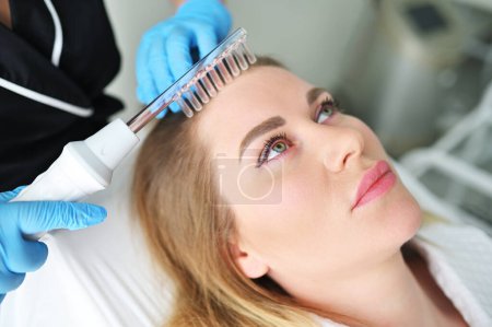 Un tricólogo dermatólogo realiza el procedimiento con un dispositivo darsonval para mejorar la condición y la calidad del cabello de los pacientes..