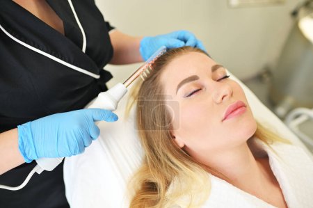 A dermatologist trichologist performs the procedure with a darsonval device to improve the condition and quality of the patients hair.