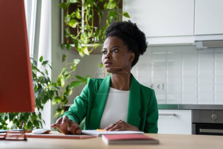 Téléchargez les photos : Concentré sur la tâche Femme d'affaires africaine travaillant sur ordinateur, assis au bureau dans la cuisine à la maison. Entrepreneure indépendante exploitant une entreprise à domicile. Travail indépendant et indépendant - en image libre de droit