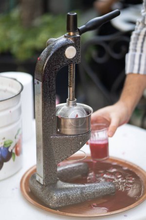 Photo for Close up process of squeezing pomegranate using manual mechanical juicer to obtain useful vitamins from natural product. Hands of seller from farmers market who extrude fresh fruit juice into glass - Royalty Free Image