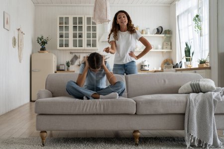 Photo for Strict mother scolding unhappy teenage daughter at home, mom lecturing teen girl, child sitting on sofa feeling afraid covering ears with hands. Parental harsh discipline, adolescent problem behavior - Royalty Free Image