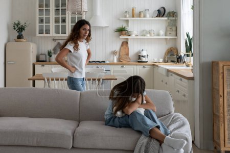 Photo for Toxic mother verbally abusing child, arguing with kid at home, sad depressed girl daughter sitting on sofa hugging pillow and crying while mom scolding her. Difficult mother-daughter relationship - Royalty Free Image