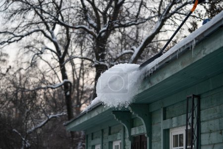 Dach mit Schaufel vom Schnee befreien. Verletzungsgefahr durch Schnee oder herabfallende Eiszapfen. Arbeiter räumen Schnee von alten Holzgebäuden. Winterdienst- und Aktivitätskonzept