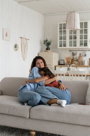 Téléchargez les photos : Happy family at home. Loving mother bonding with teenage daughter on weekend, mom hugging embracing teen girl adolescent kid while resting on sofa in living room. Healthy parent-child relationship - en image libre de droit