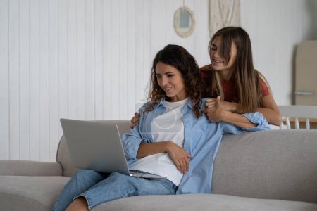 Photo for Happy smiling European family of woman and teen girl watching interesting video in laptop and laughing. Cheerful positive daughter hugs mother sits on couch and enjoys watching favorite series at home - Royalty Free Image