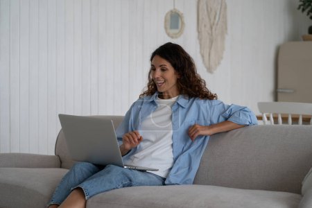 Photo for Excited contented woman on sofa with laptop on lap laughing watching comedy video or youth series sits in living room. Cheerful impressed lady use portable computer to relax after hard days work - Royalty Free Image