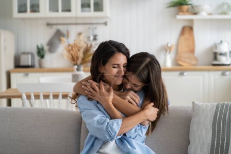 Photo for Happy smiling family of young mother and teenage daughter spending time together at home. Loving bored girl hugs woman sits on couch clinging to from behind feeling affection and not wanting to part - Royalty Free Image