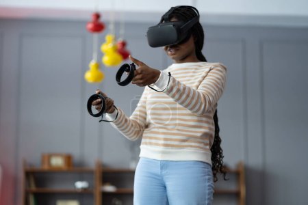 Téléchargez les photos : Exciter femme noire tester dispositif de réalité virtuelle dans le monde numérique. Collège étudiant fille tenir contrôleurs jouer jeu vidéo de tir vr futuriste simulateur immersif réalité virtuelle 3D 360 cyber jeu - en image libre de droit