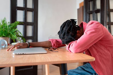 Photo for Exhausted overloaded African guy remote worker sleeping on desk while working remotely from home, suffering from freelancer burnout. Student guy experiencing sleep deprivation from virtual learning - Royalty Free Image