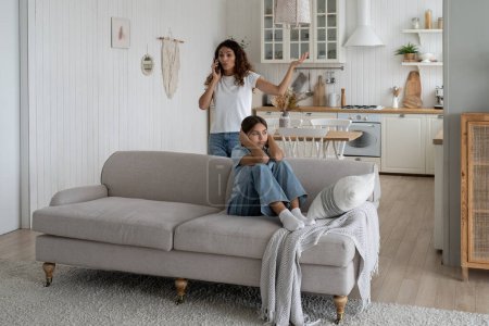 Foto de Nervous mother arguing with husband over phone in front of daughter child at home, stressed frustrated teen girl kid covering ears while her mom talking on mobile with dad about her bad behavior - Imagen libre de derechos